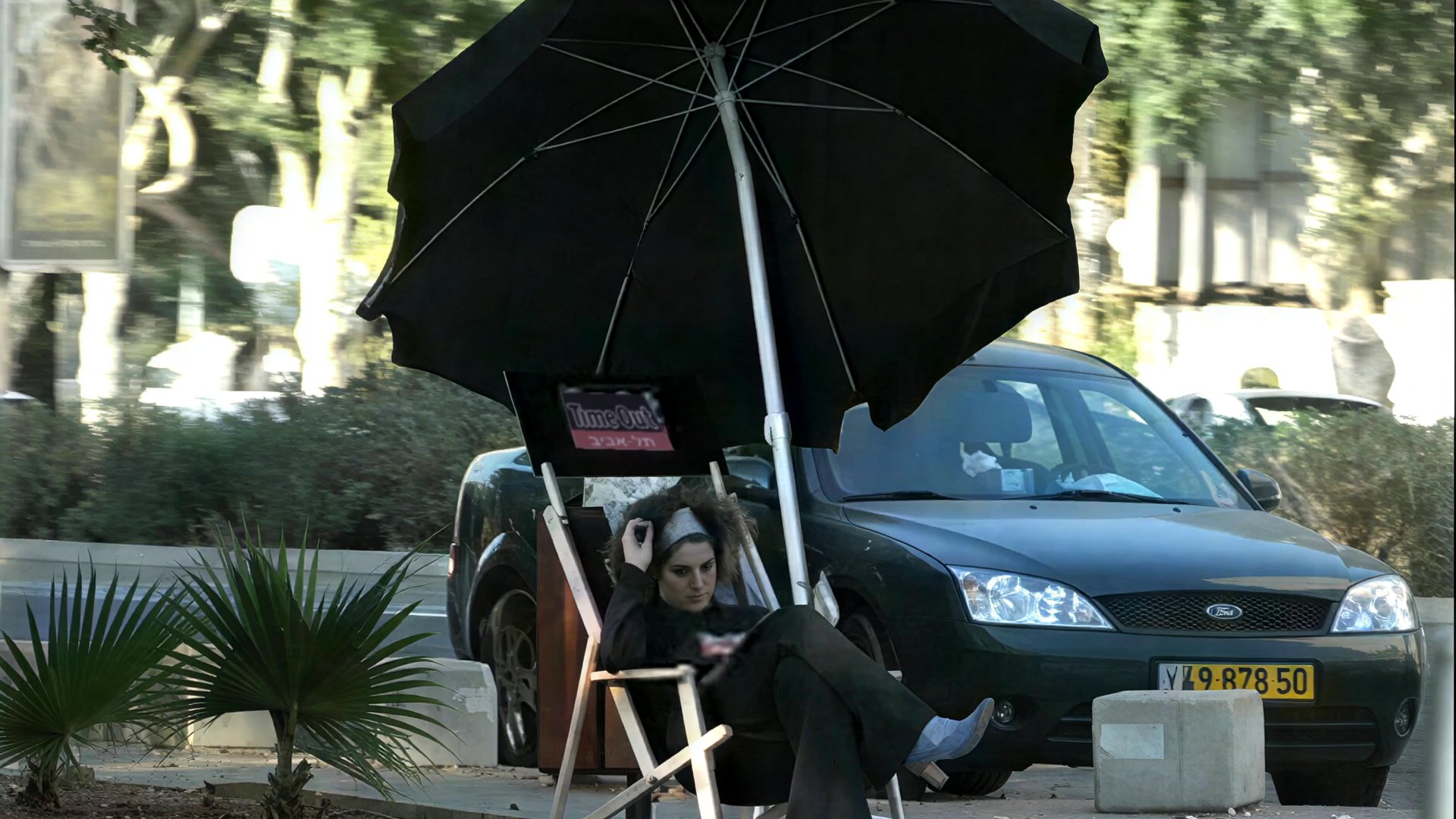 A promoter on a deckchair under a Time Out umbrella on a traffic island, a car right behind her
